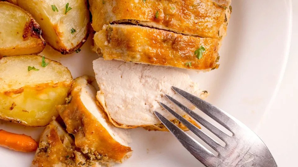 Sliced oven roasted whole chicken on a plate with roasted potatoes and a fork.